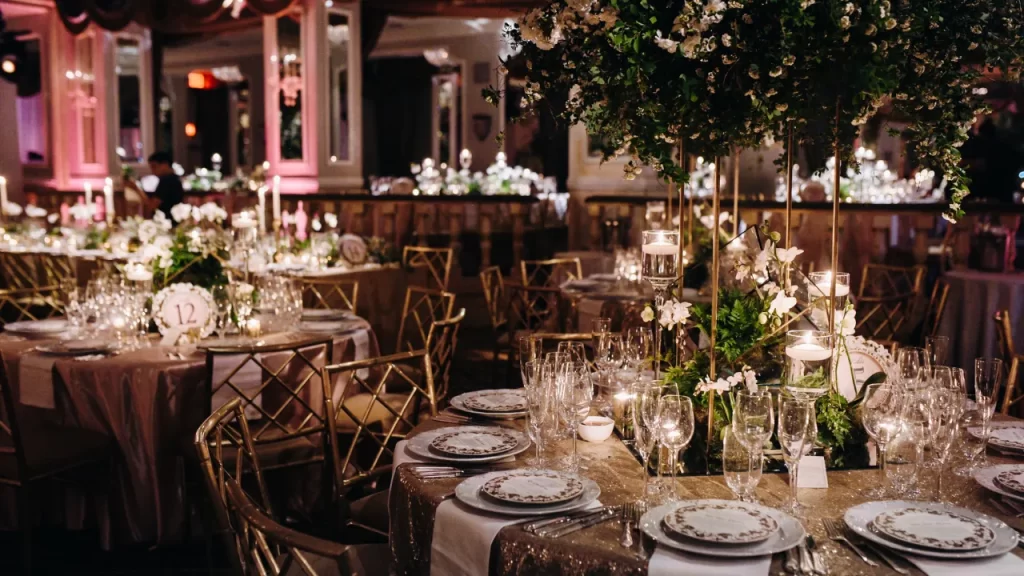 Salão de festas sofisticado com mesas redondas decoradas, arranjos florais elegantes e iluminação com velas.